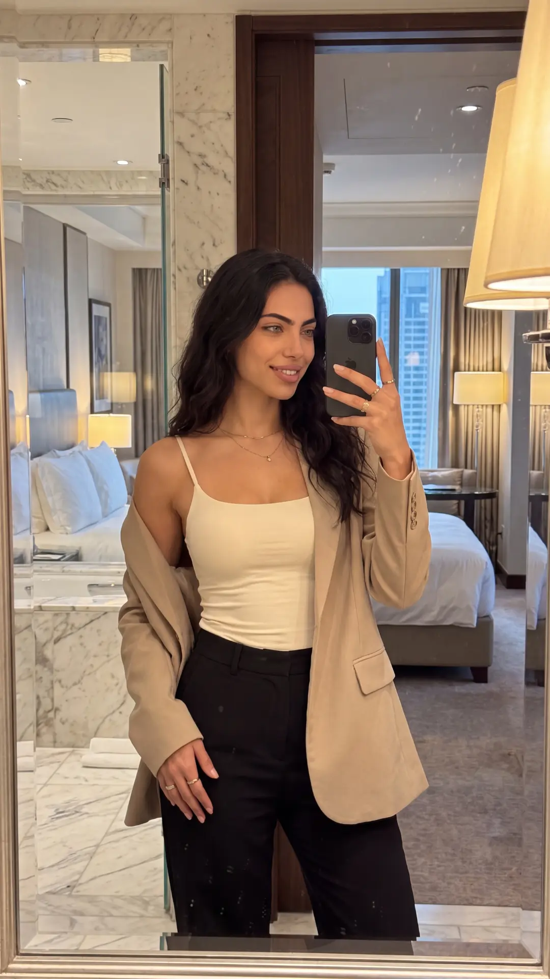 Sera Lanes in a beige blazer taking a mirror selfie in a hotel room