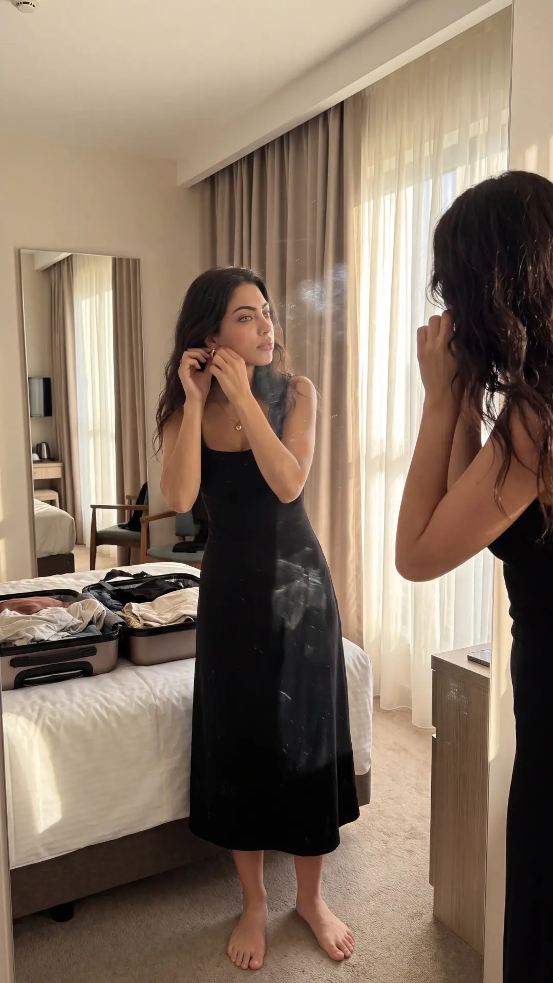 Sera Lanes fastening an earring in a hotel room mirror, wearing a black dress